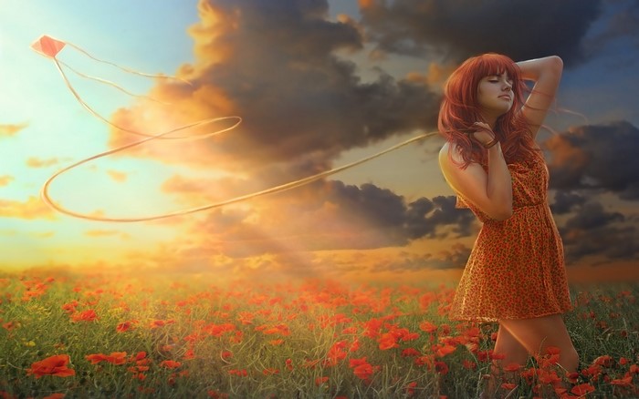 Girl flying a kite in a poppy field at sunset