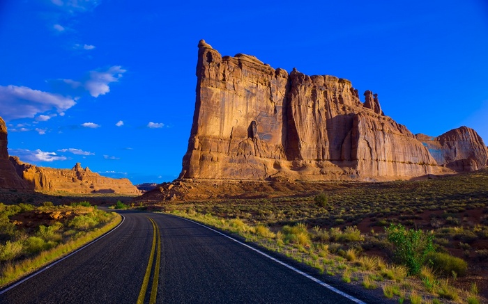 Desert road leading to sandstone formations under blue sky