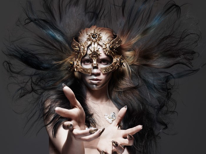 Grimes wearing a gold mask with elaborate hair