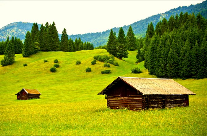 Wooden cabins in a green meadow with forests and mountains