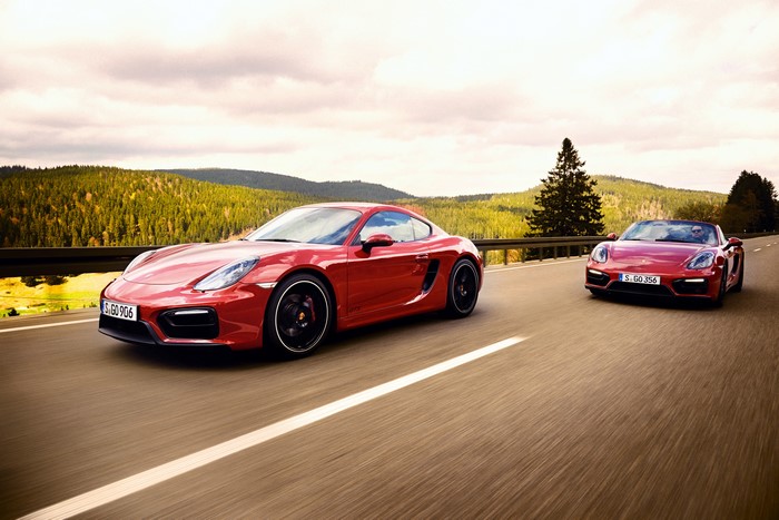 Two red Porsche cars driving on a road