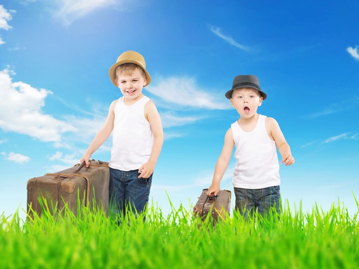 Two boys with suitcases and hats in grass