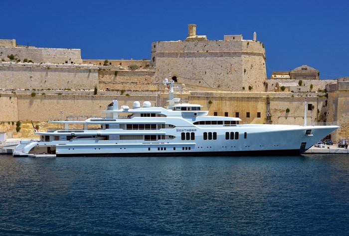 White luxury yacht docked near historic stone fortress