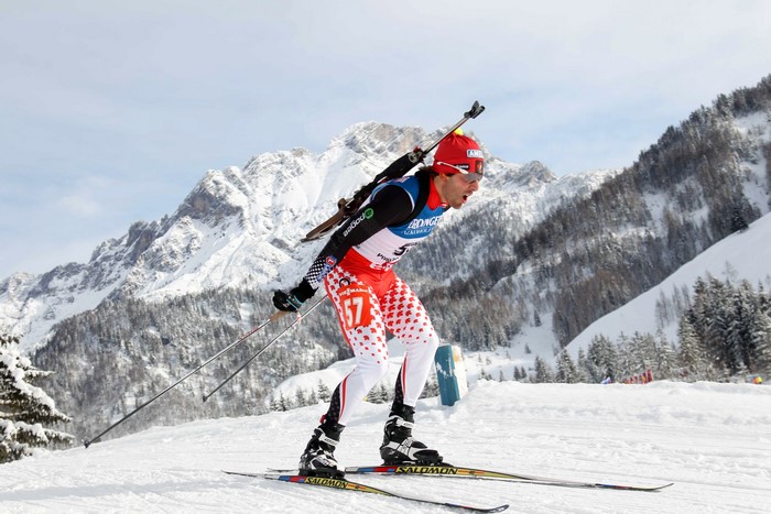 Biathlete skiing with rifle in snowy mountains