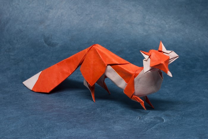 Orange and white origami fox on blue background