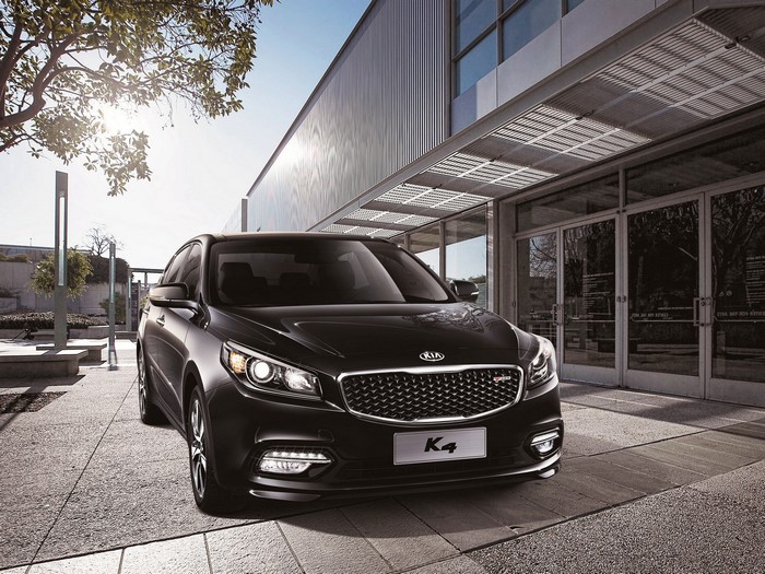 Black 2014 Kia K4 parked in front of a modern building