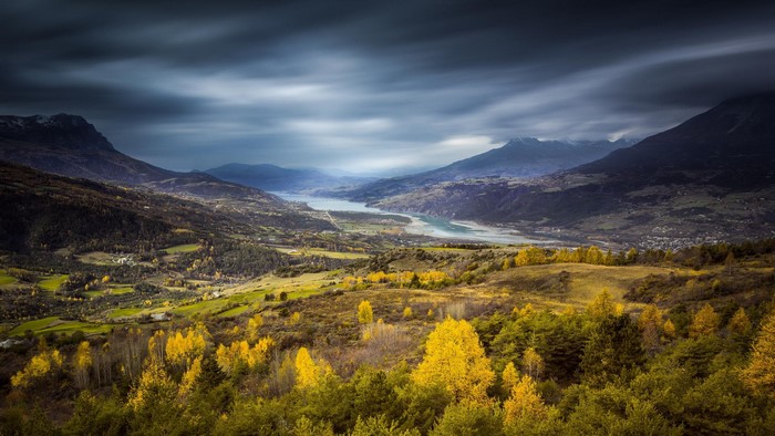 Autumn valley with a river and mountains under stormy sky
