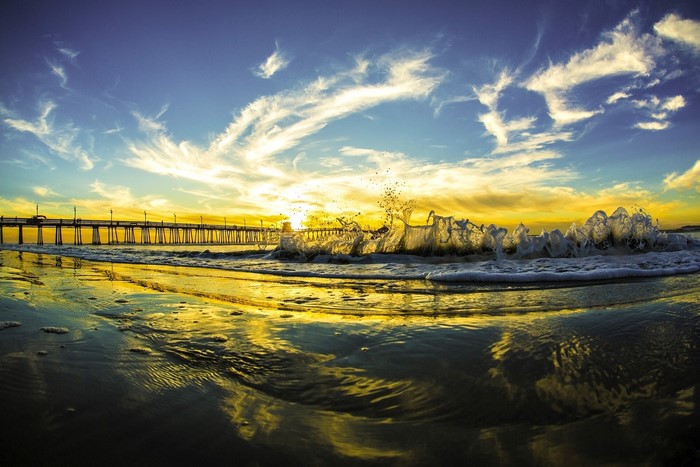 Ocean wave crashing near a pier at sunset