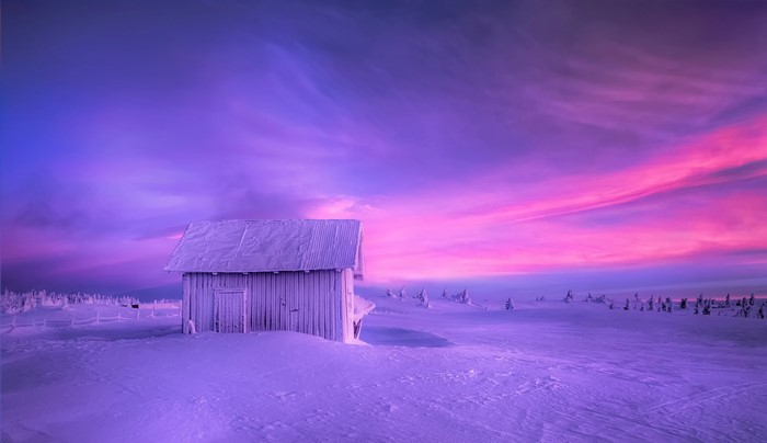 Wooden cabin in a snowy landscape under a purple and pink sky