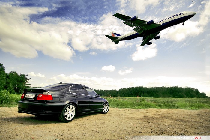 Black BMW sedan parked under a Transaero airplane in the sky