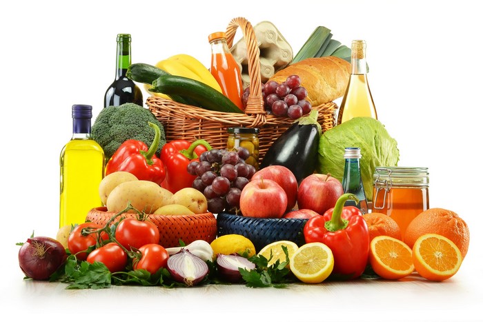 Assortment of fresh fruits, vegetables, and bottles in a wicker basket