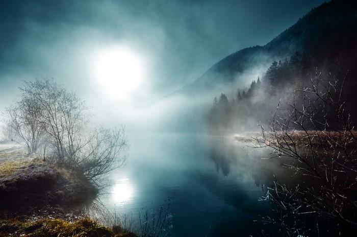 Misty lake with sun and mountains at night