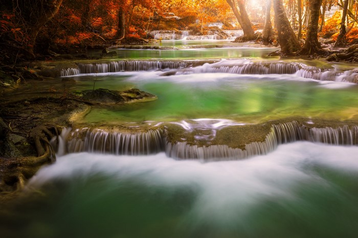 Tiered waterfalls with autumn foliage and sunlight