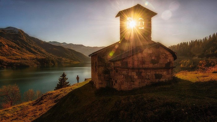 Stone church with sun rays over a lake and mountains