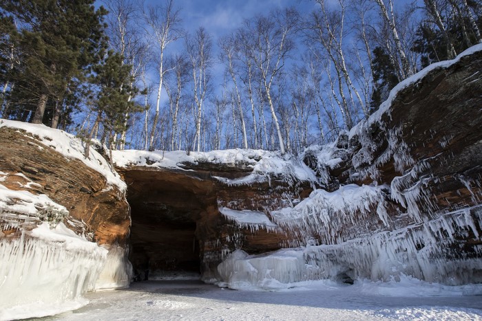 Winter cave with ice formations and birch trees