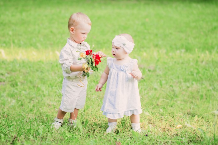 Boy giving flowers to a baby girl in grass