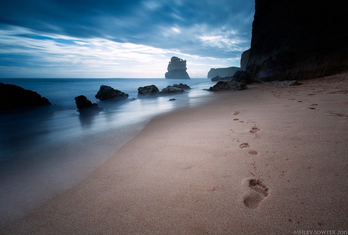 Footprints on a sandy beach with rock formations in the sea