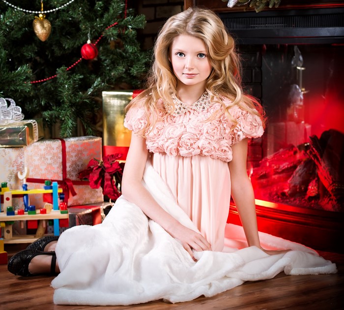 Girl in a pink dress by a Christmas tree and fireplace