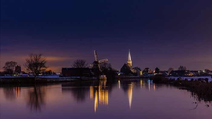 Windmill and church by canal at night in Netherlands