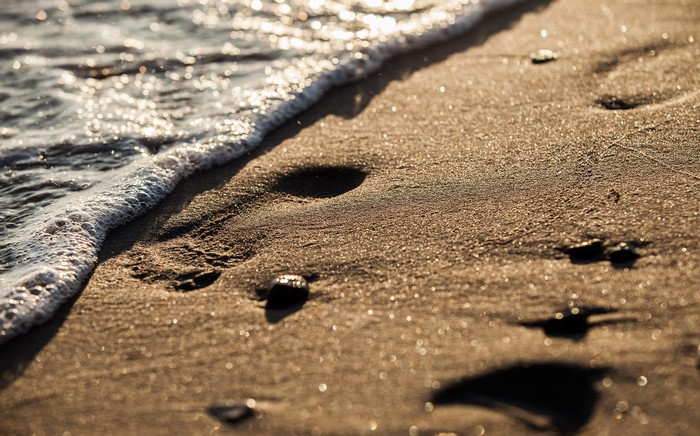 Close-up of waves washing over sandy beach with footprints