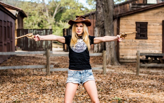 Woman in cowboy hat holding revolvers
