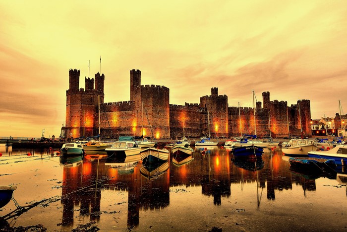 Caernarfon Castle and boats in a harbor at dusk