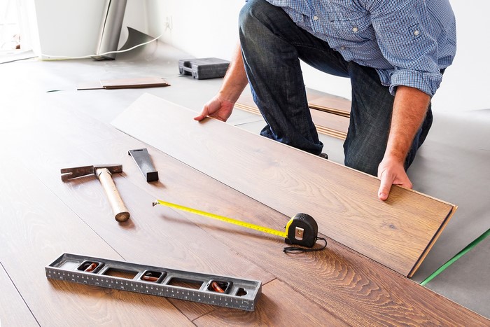 Worker installing laminate flooring with tools