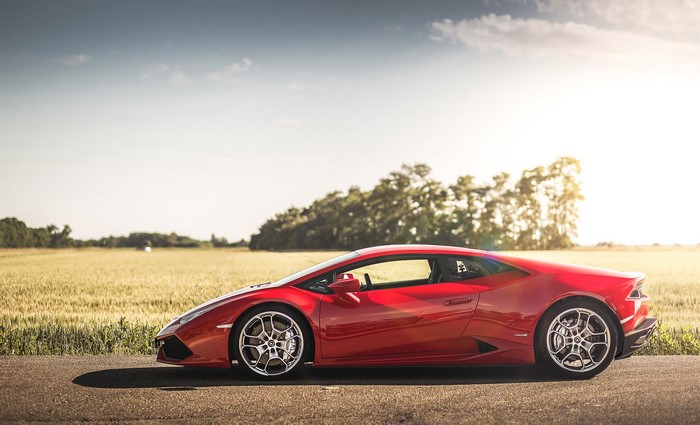 Red Lamborghini parked on a road with a field