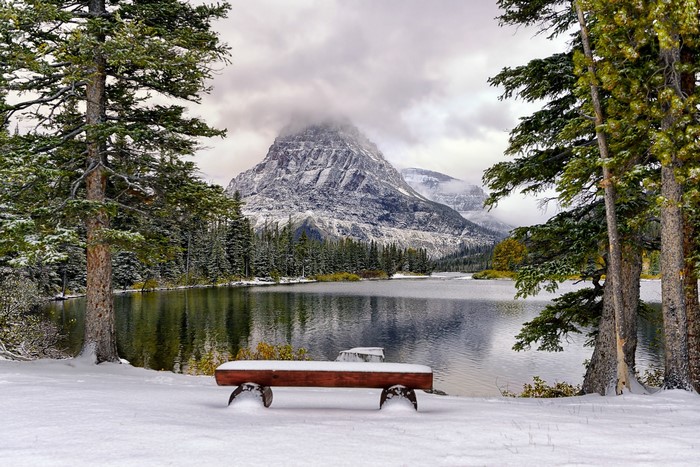 Snowy mountain lake with trees and bench