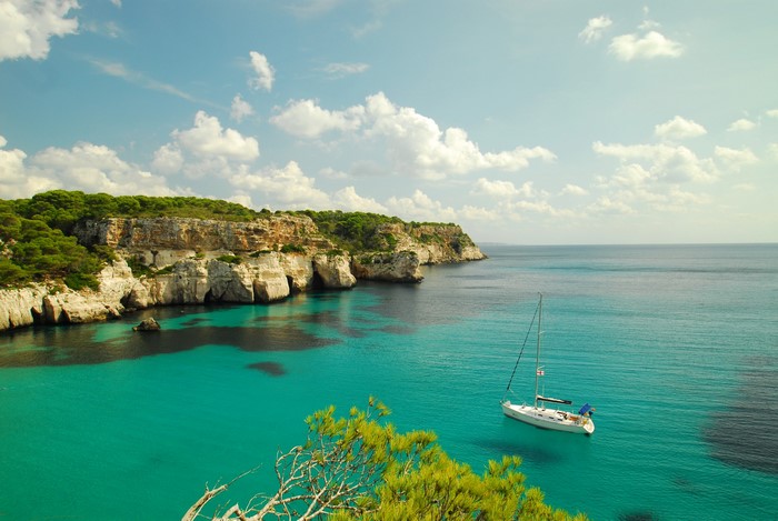 Sailboat in a turquoise bay with cliffs and trees