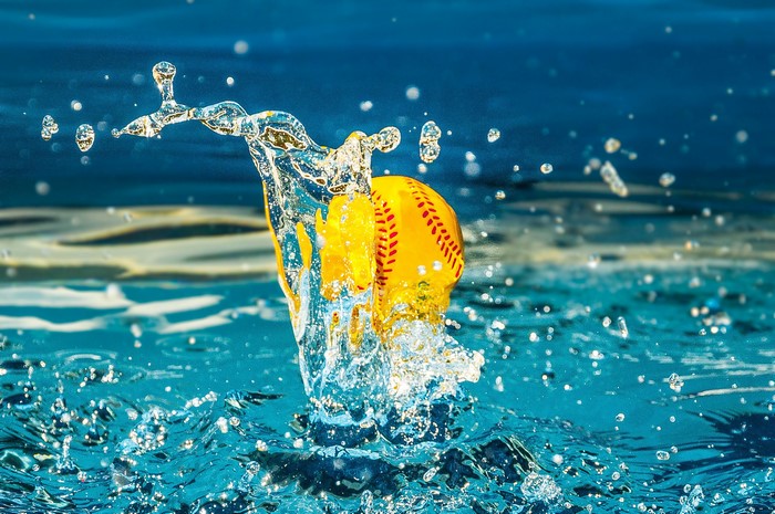 Yellow softball splashing into blue water