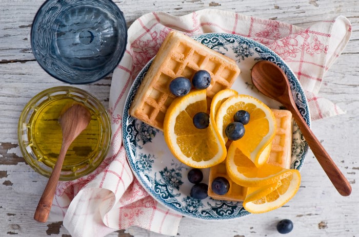 Waffles with blueberries and orange slices, honey, and a blue glass