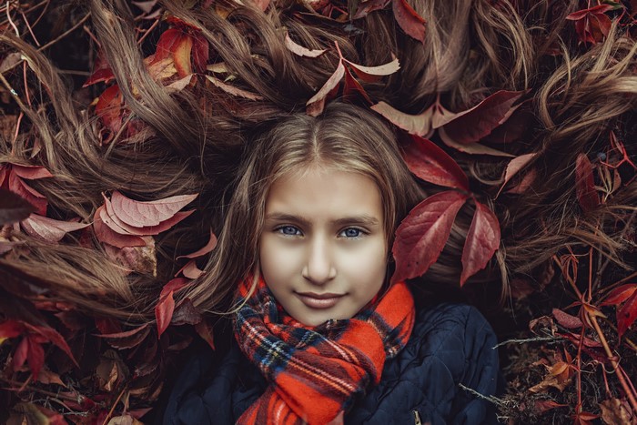 Girl with brown hair lying in autumn leaves