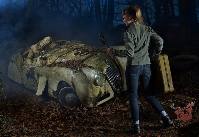 Woman with suitcase and wrench near abandoned car in forest