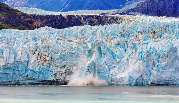 Glacier calving into the sea with mountains in background