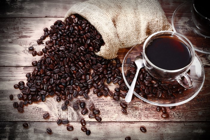 Coffee beans spilling from a burlap sack next to a cup of coffee