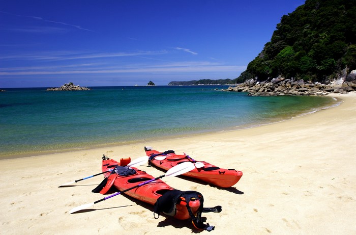 Two red kayaks on a sandy beach with turquoise water and green hills