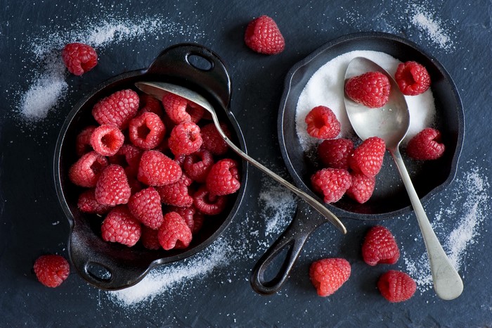 Raspberries and sugar in cast iron dishes with spoons
