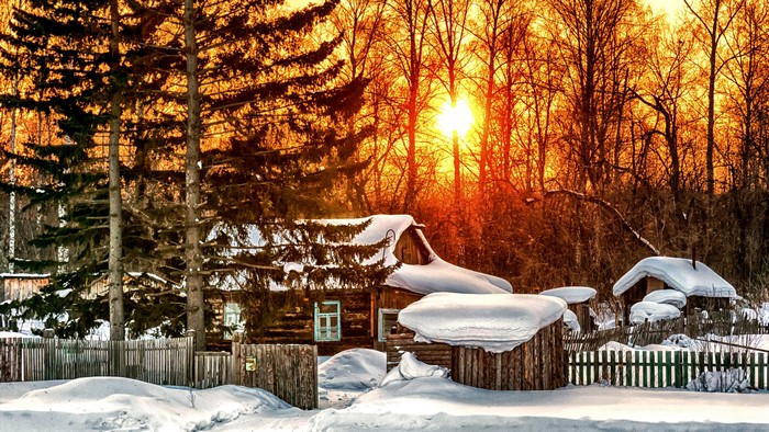 Winter scene with snow-covered houses and trees at sunset