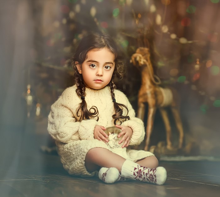 Girl in sweater holding snow globe near Christmas tree