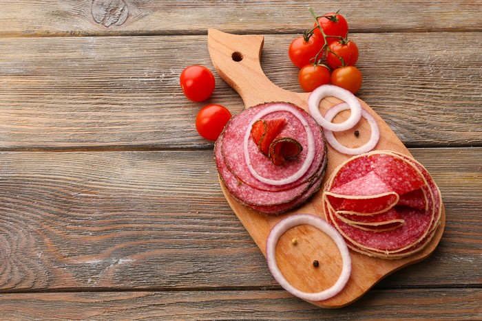 Sausage slices with tomatoes and onion rings on a cutting board