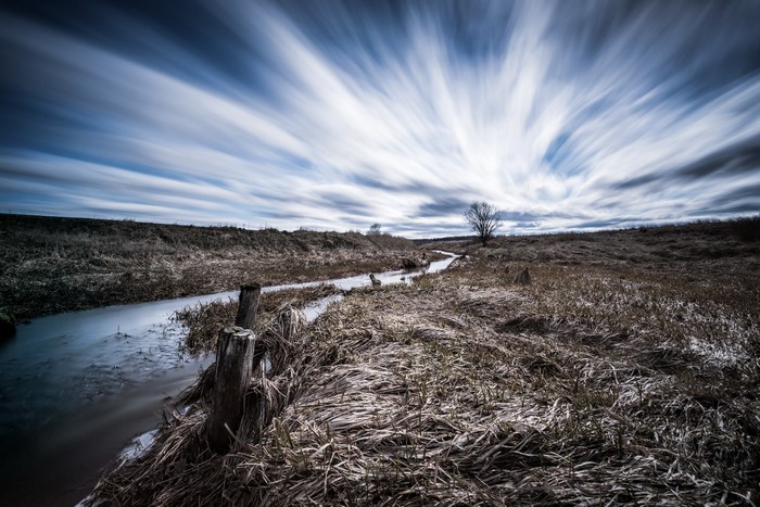 Long exposure of a stream in a field under a streaky sky