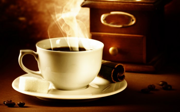 Coffee cup with steam, sugar cube, cinnamon, and coffee beans