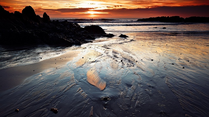 Sunset over a rocky beach with wet sand