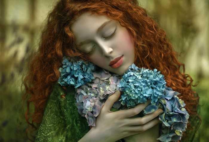 Redhead girl with curly hair holding blue hydrangeas