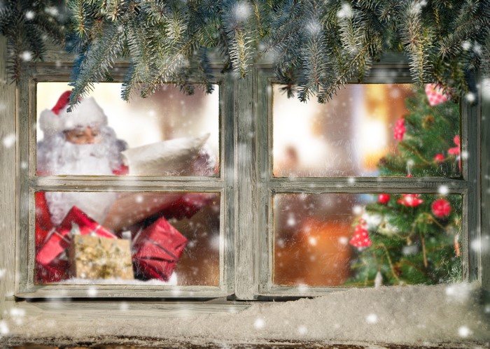 Santa Claus looking through a snowy window with gifts and a Christmas tree