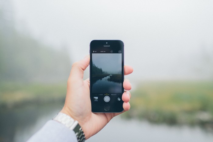 Hand holding iPhone taking picture of foggy landscape