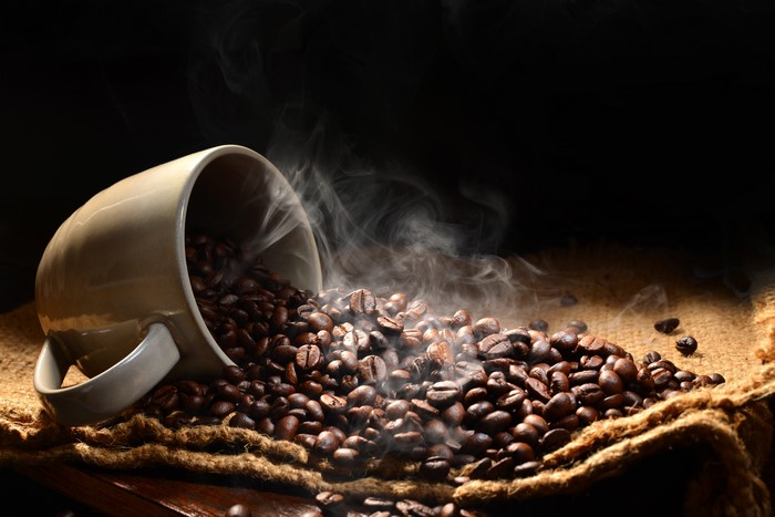 Coffee beans spilling from a cup with steam