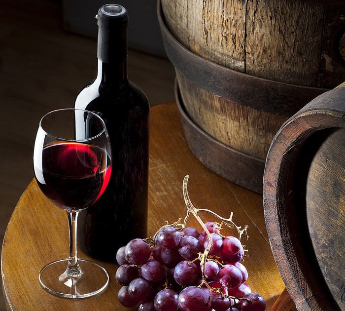 Red wine in a glass and bottle with grapes and barrels