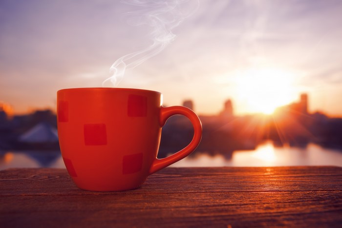 Red coffee cup with steam at sunrise